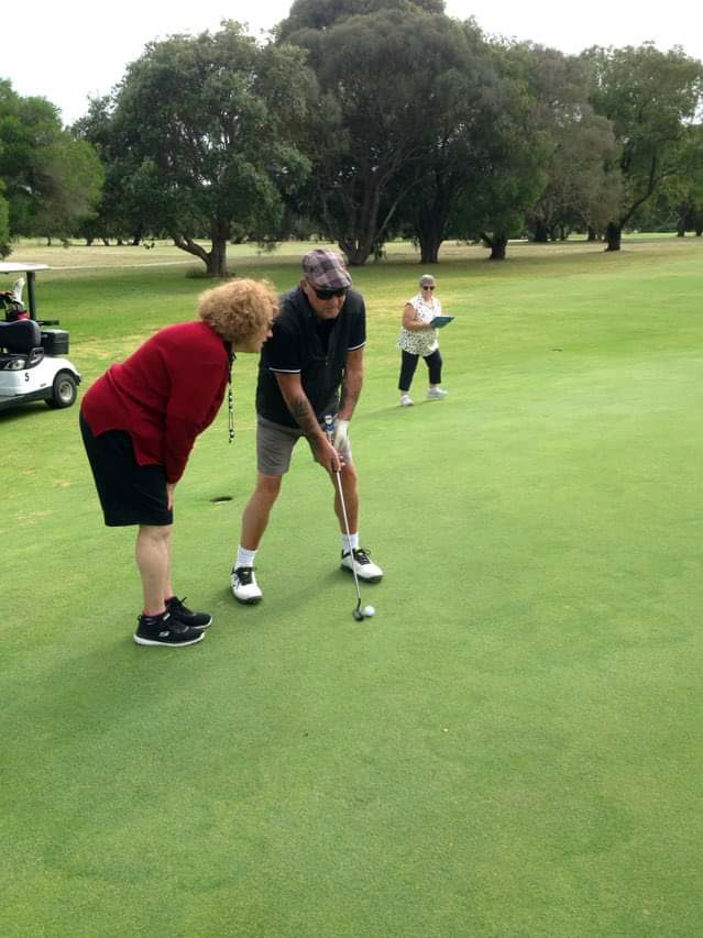 Photo of Doug Sloan playing Blind Golf on the green lining up a putt with the aid of verbal instructions from his caddie